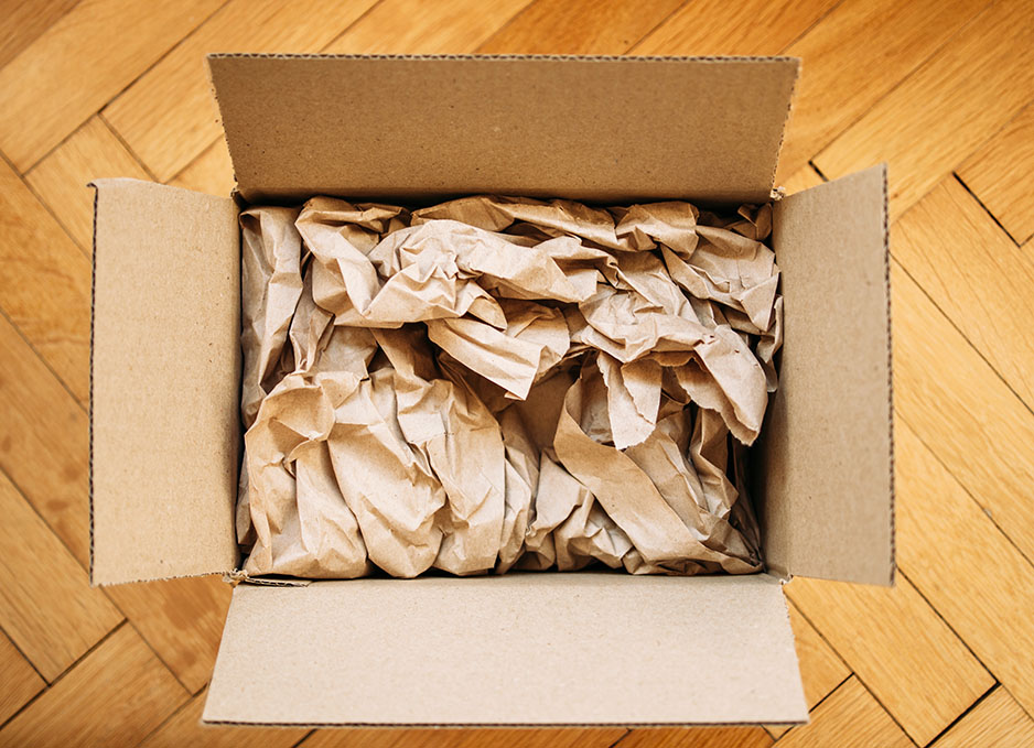 Cardboard box filled with shipping packaging paper on a wood floor