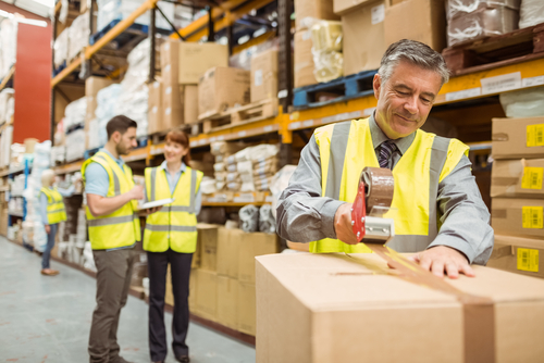 Warehouse worker sealing cardboard boxes for shipping in a large warehouse
