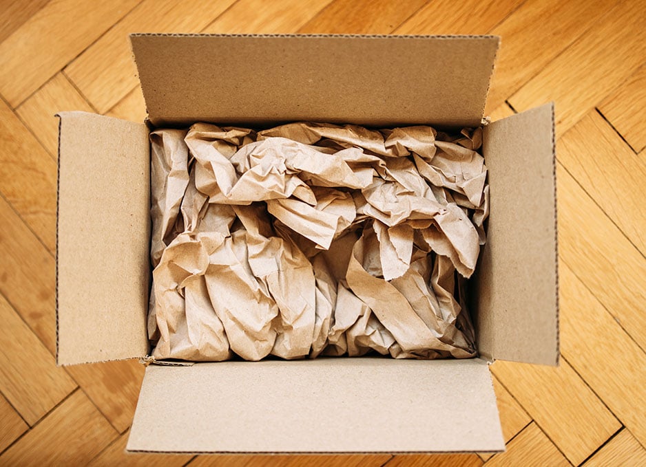 Cardboard box filled with shipping packaging paper on a wood floor